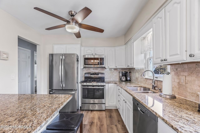 kitchen with sink, hardwood / wood-style flooring, white cabinetry, stainless steel appliances, and light stone counters