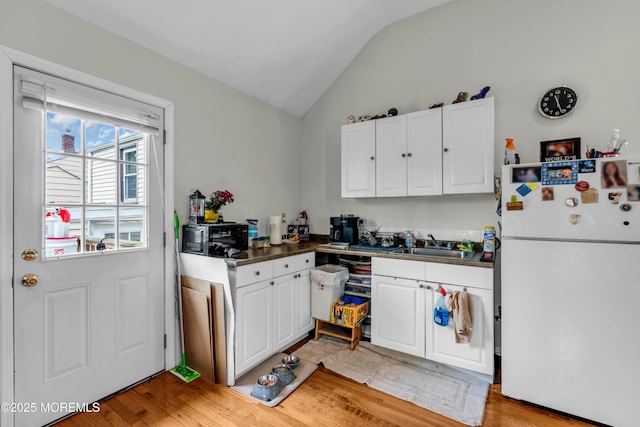 kitchen with lofted ceiling, freestanding refrigerator, light wood-type flooring, white cabinetry, and a sink