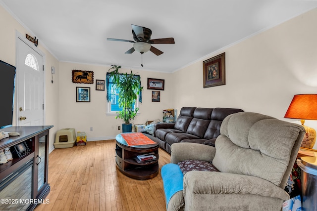 living area with ornamental molding, light wood-type flooring, a ceiling fan, and baseboards