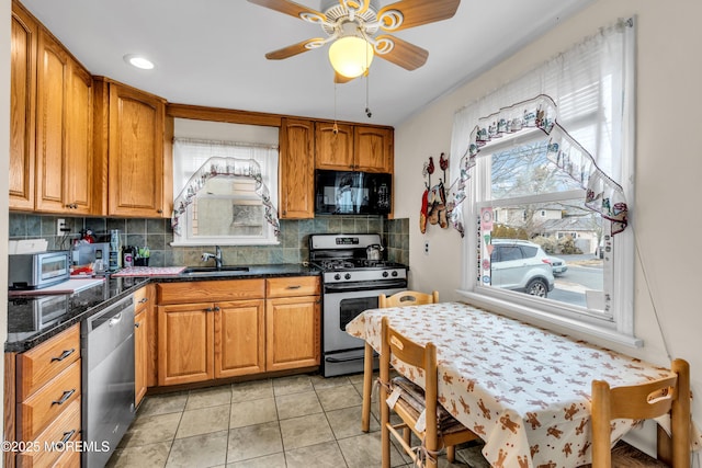 kitchen featuring brown cabinets, stainless steel appliances, backsplash, a ceiling fan, and a sink