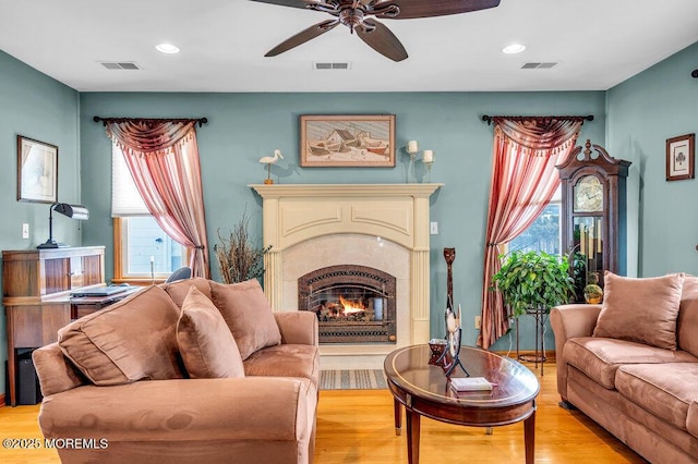 living room with ceiling fan, a fireplace, and light hardwood / wood-style floors