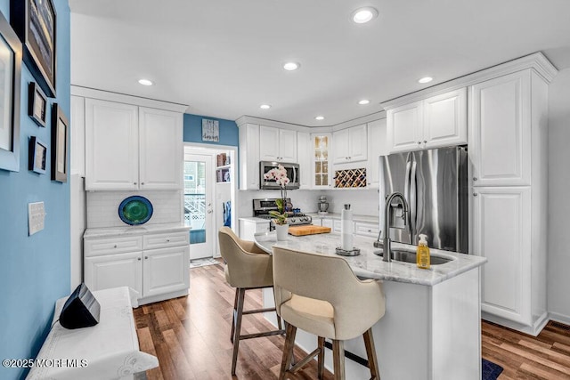 kitchen with appliances with stainless steel finishes, a kitchen island with sink, dark hardwood / wood-style floors, light stone counters, and white cabinets