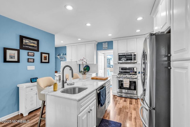 kitchen with sink, stainless steel appliances, an island with sink, and white cabinets