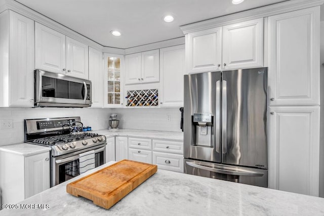 kitchen featuring tasteful backsplash, light stone counters, stainless steel appliances, and white cabinets