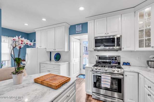 kitchen featuring appliances with stainless steel finishes, light wood-type flooring, decorative backsplash, and white cabinets