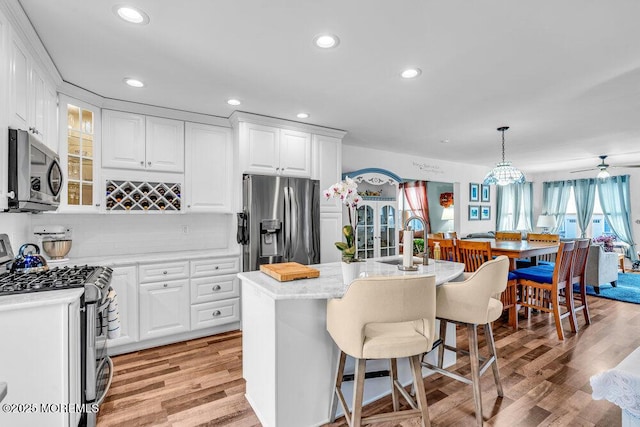 kitchen with appliances with stainless steel finishes, decorative light fixtures, a center island with sink, and white cabinets