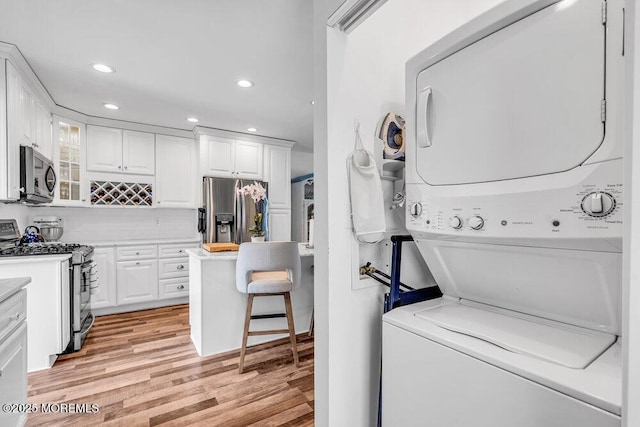 laundry area featuring stacked washer / drying machine and light wood-type flooring