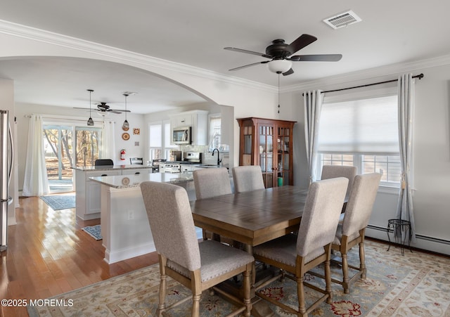 dining space featuring crown molding, light hardwood / wood-style floors, ceiling fan, and baseboard heating