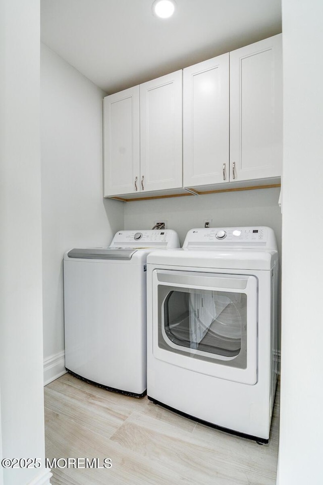 laundry area with cabinets, washer and clothes dryer, and light hardwood / wood-style flooring