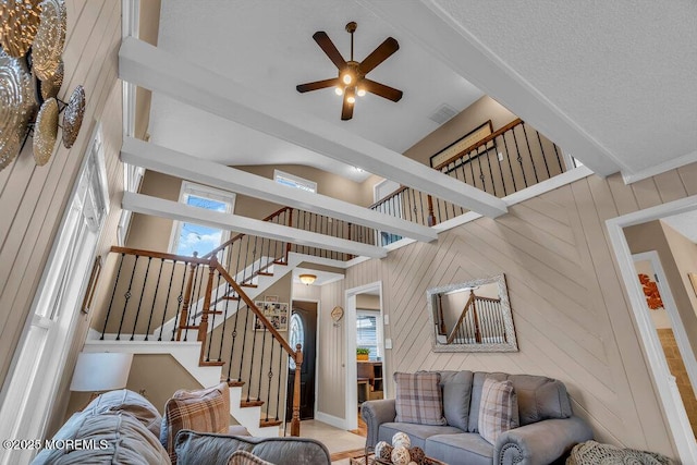 living room with ceiling fan, high vaulted ceiling, beam ceiling, and wood walls