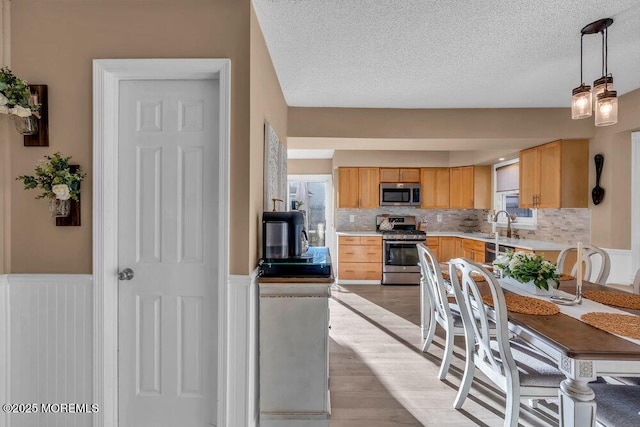 kitchen featuring a textured ceiling, light wood-type flooring, light brown cabinets, pendant lighting, and stainless steel appliances