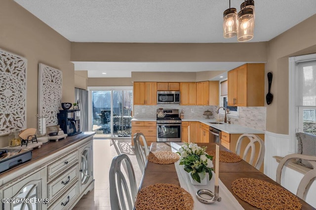 kitchen featuring sink, stainless steel appliances, tasteful backsplash, light brown cabinetry, and decorative light fixtures