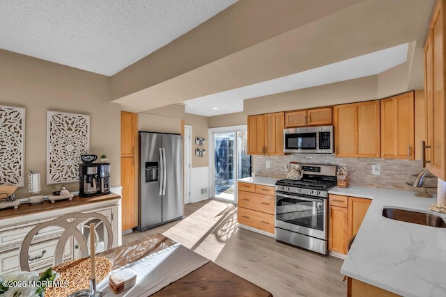 kitchen featuring sink, light wood-type flooring, decorative backsplash, stainless steel appliances, and a textured ceiling