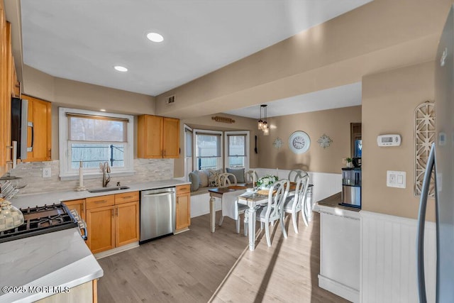 kitchen featuring appliances with stainless steel finishes, sink, backsplash, hanging light fixtures, and light hardwood / wood-style flooring