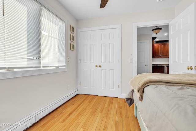 bedroom with hardwood / wood-style flooring, ceiling fan, baseboard heating, and a closet