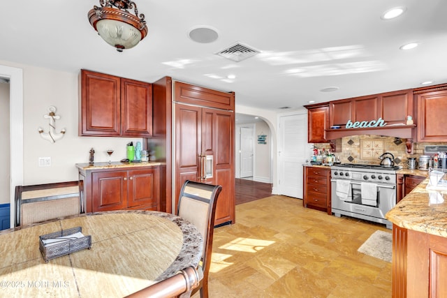 kitchen with light stone countertops, high end stainless steel range, and decorative backsplash