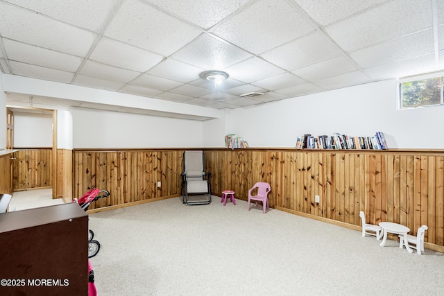 interior space with a paneled ceiling, wooden walls, light colored carpet, visible vents, and wainscoting