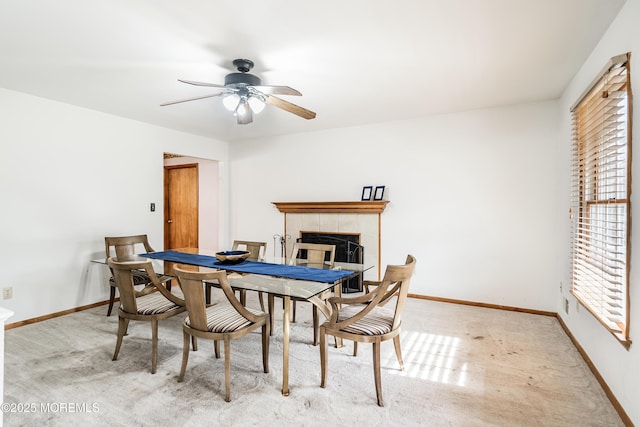 dining area featuring light carpet, a tiled fireplace, baseboards, and a ceiling fan