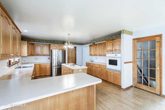 kitchen with decorative light fixtures, light countertops, a sink, white appliances, and a peninsula