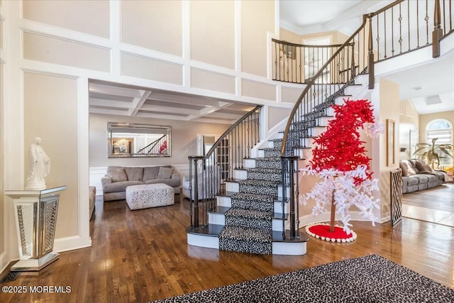 stairs with hardwood / wood-style flooring, a towering ceiling, coffered ceiling, and beamed ceiling