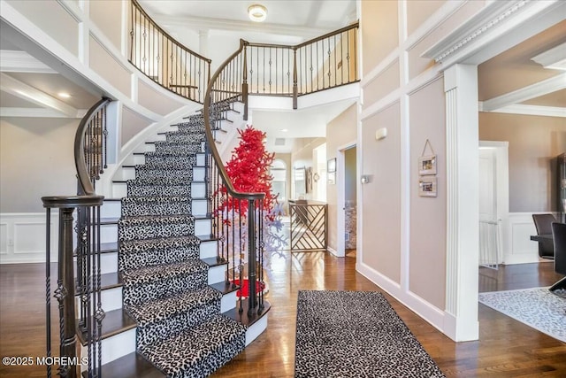 stairs with ornamental molding, wood-type flooring, and a towering ceiling