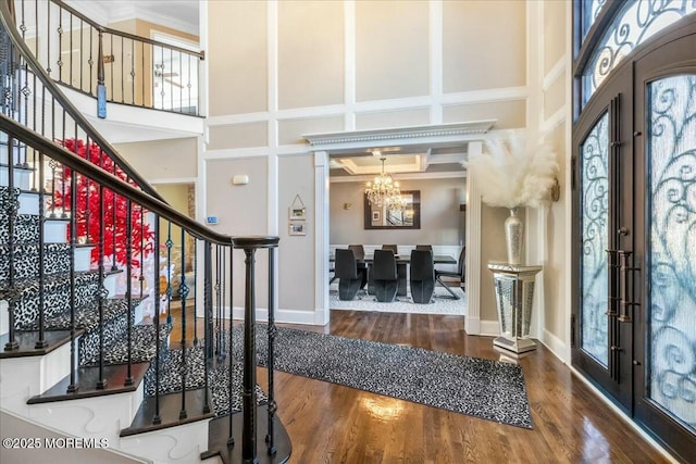 foyer entrance featuring french doors, an inviting chandelier, ornamental molding, a towering ceiling, and hardwood / wood-style floors