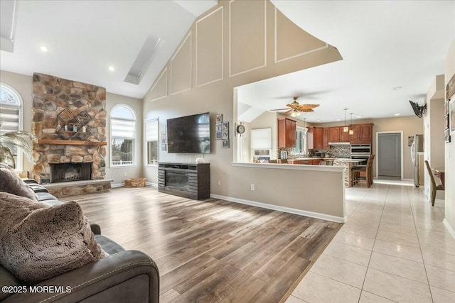 living room featuring ceiling fan, a fireplace, high vaulted ceiling, and light hardwood / wood-style flooring