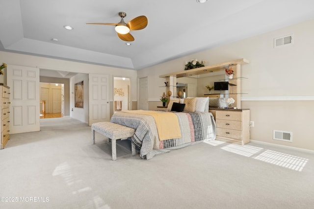 bedroom with ceiling fan, light colored carpet, ensuite bath, and a tray ceiling