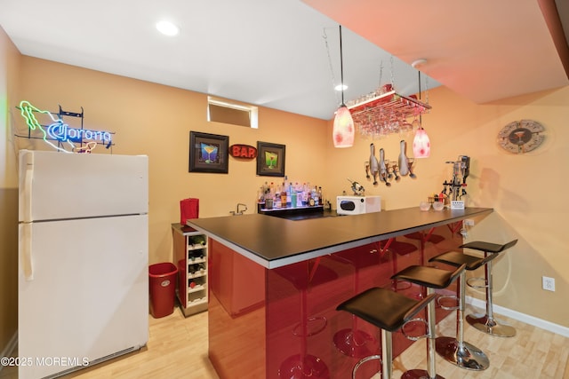 bar featuring hanging light fixtures, white appliances, and light hardwood / wood-style floors