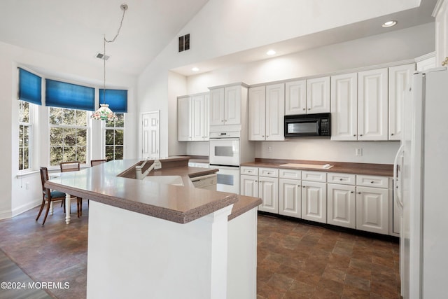 kitchen with sink, high vaulted ceiling, hanging light fixtures, white appliances, and white cabinets