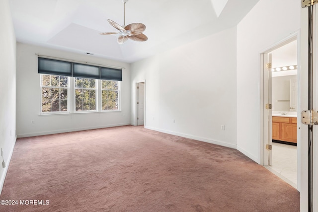 interior space with light carpet, a tray ceiling, and ensuite bathroom