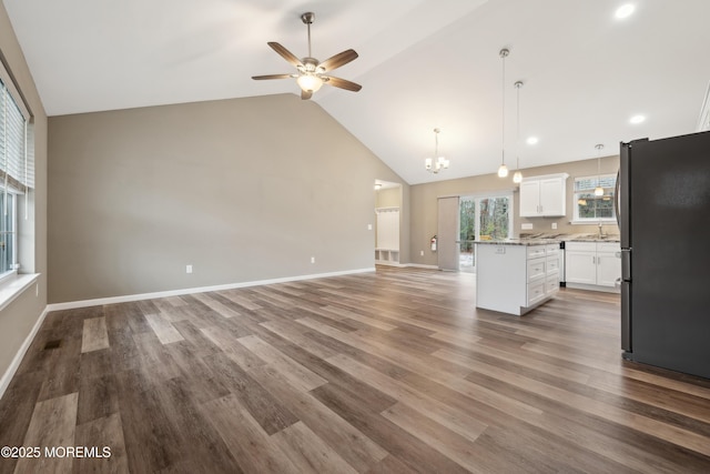 unfurnished living room with ceiling fan with notable chandelier, high vaulted ceiling, hardwood / wood-style flooring, and sink