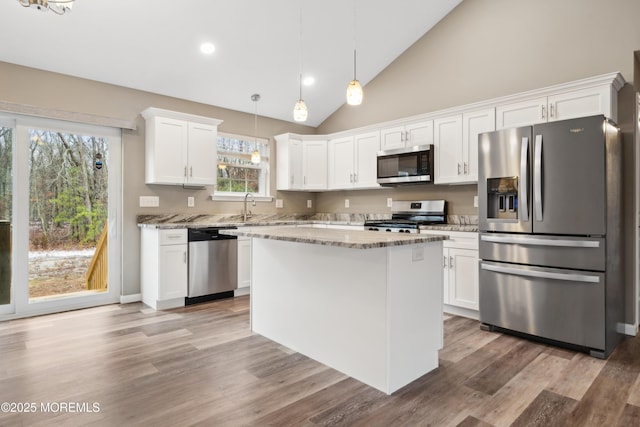 kitchen with a kitchen island, decorative light fixtures, stainless steel appliances, white cabinets, and light stone countertops