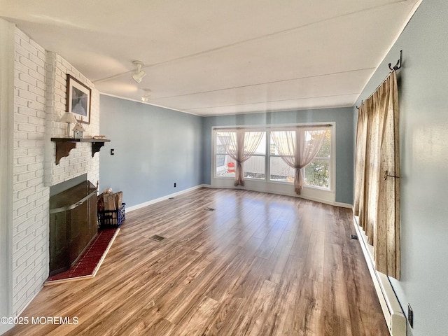 unfurnished living room with baseboard heating, wood-type flooring, and a brick fireplace