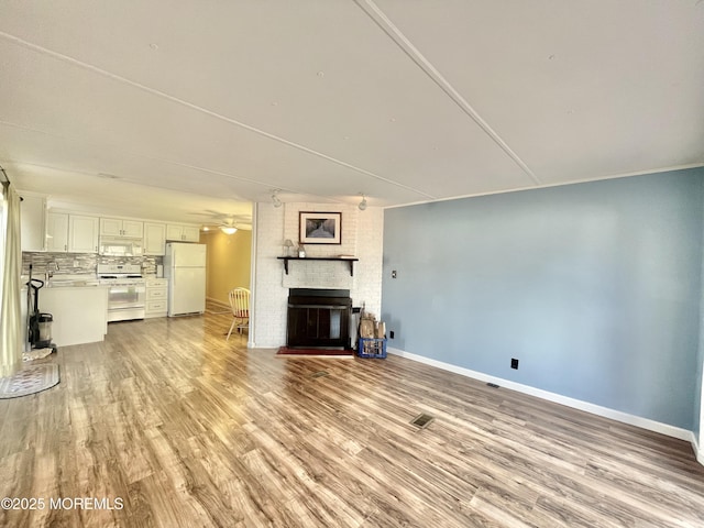 unfurnished living room with a brick fireplace, ceiling fan, and light wood-type flooring