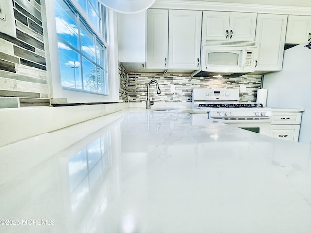 kitchen with sink, white appliances, white cabinetry, backsplash, and light stone countertops