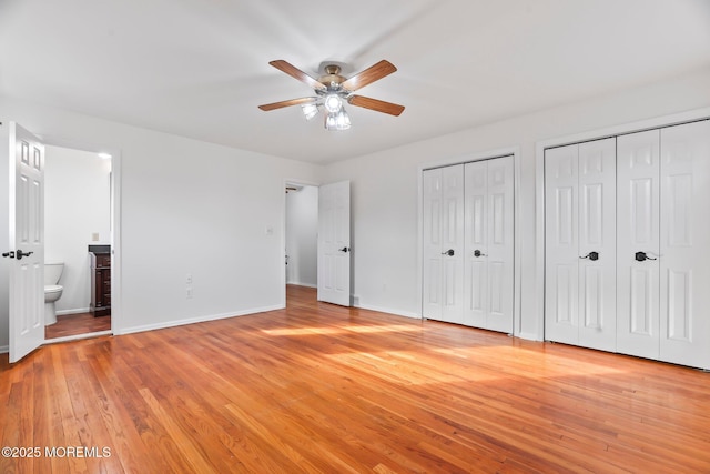 unfurnished bedroom featuring two closets, light hardwood / wood-style floors, ceiling fan, and ensuite bathroom