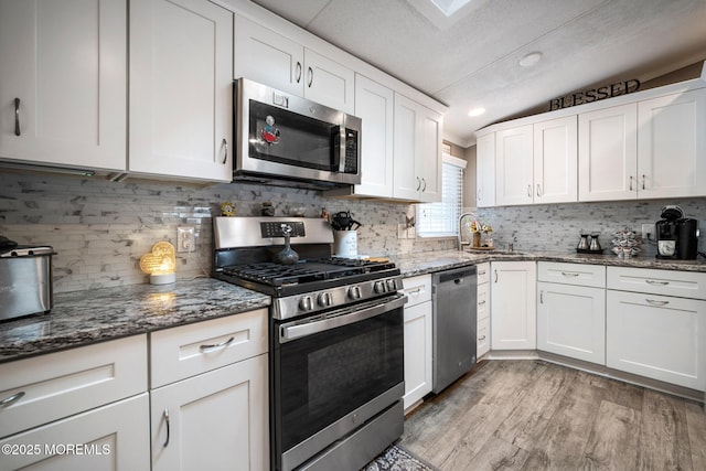 kitchen featuring stainless steel appliances, white cabinetry, dark stone countertops, and light hardwood / wood-style floors