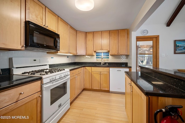 kitchen with sink, white appliances, light hardwood / wood-style flooring, dark stone countertops, and decorative backsplash