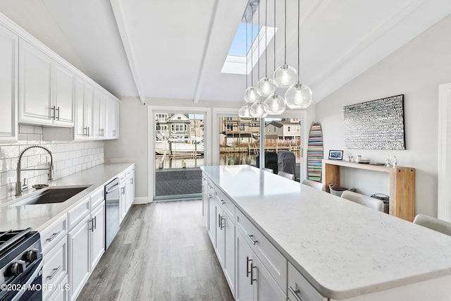 kitchen featuring vaulted ceiling with skylight, white cabinets, a kitchen island, decorative light fixtures, and stainless steel dishwasher