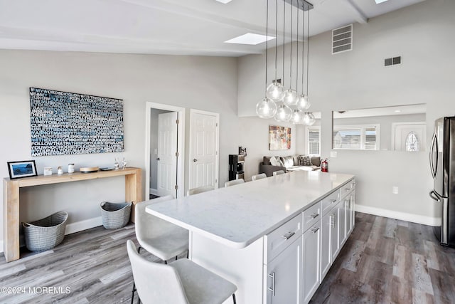 kitchen featuring a skylight, decorative light fixtures, white cabinetry, stainless steel fridge, and a center island