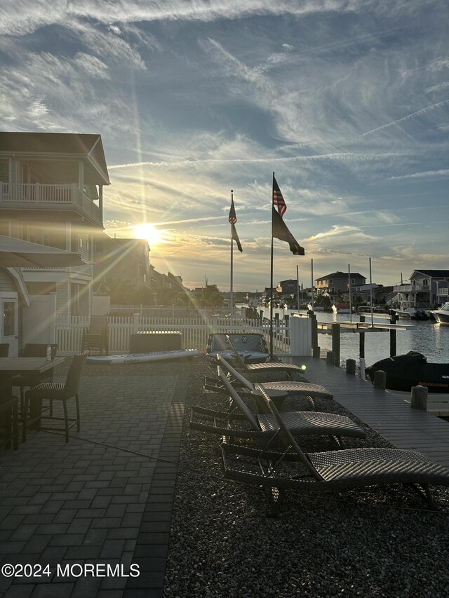 patio terrace at dusk featuring a dock and a water view