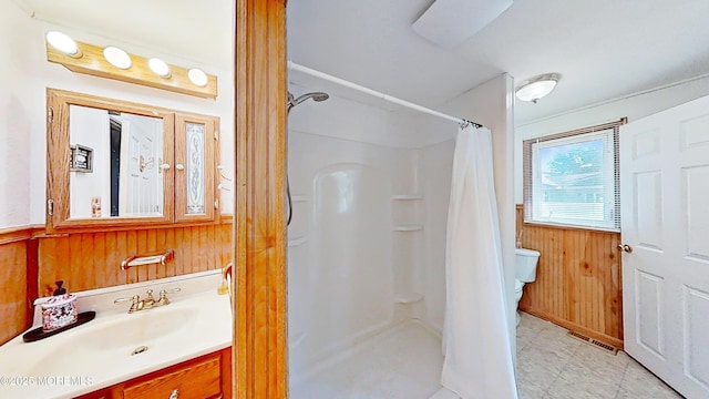 bathroom with vanity, curtained shower, wooden walls, and toilet