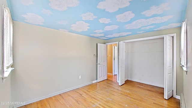 unfurnished bedroom featuring a closet, baseboard heating, and light hardwood / wood-style flooring