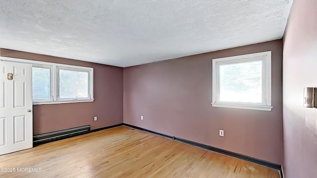 empty room featuring a baseboard heating unit, light hardwood / wood-style floors, and a textured ceiling