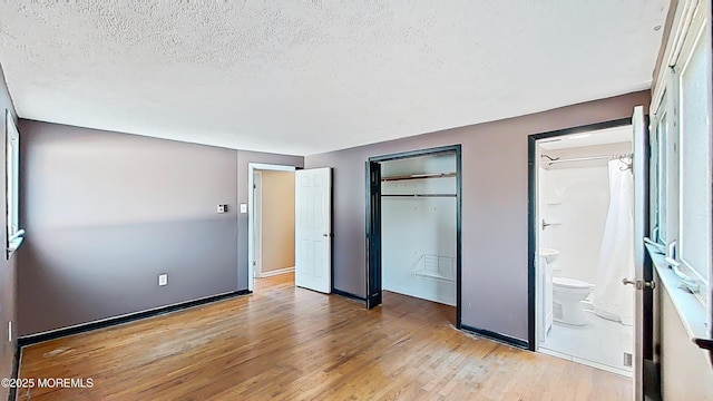 unfurnished bedroom with a closet, ensuite bathroom, light hardwood / wood-style flooring, and a textured ceiling