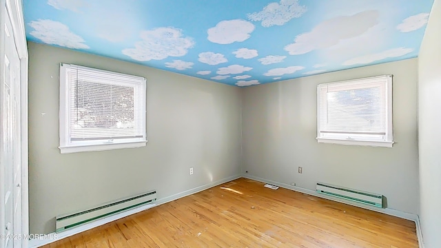 empty room featuring a healthy amount of sunlight, a baseboard heating unit, and light hardwood / wood-style floors