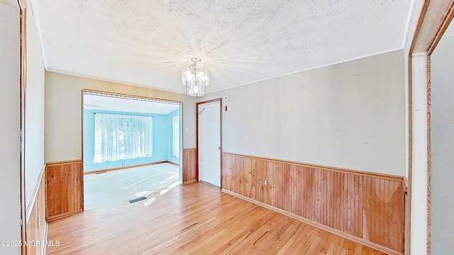 spare room featuring wooden walls, ornamental molding, a notable chandelier, a textured ceiling, and light wood-type flooring