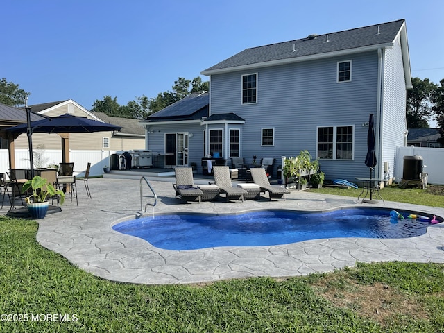 back of property with a patio, a pool with hot tub, and solar panels