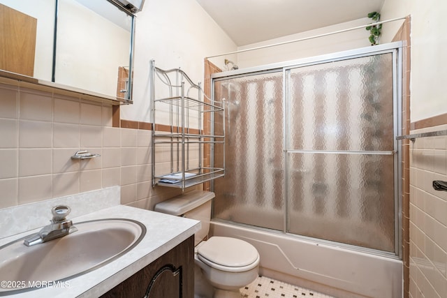 full bathroom with vanity, combined bath / shower with glass door, tile walls, and toilet